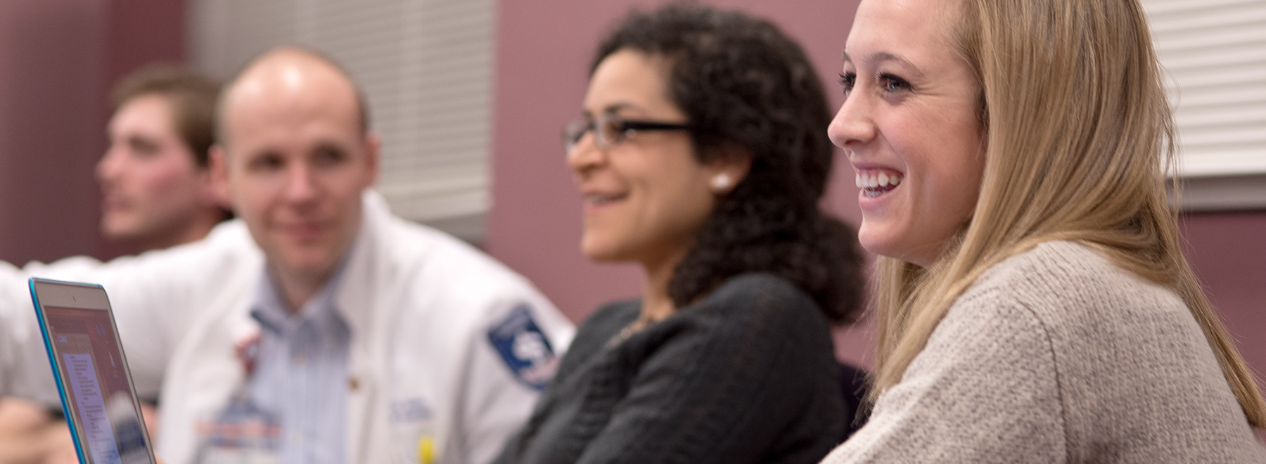 Female student smiles in class while viewing her laptop.